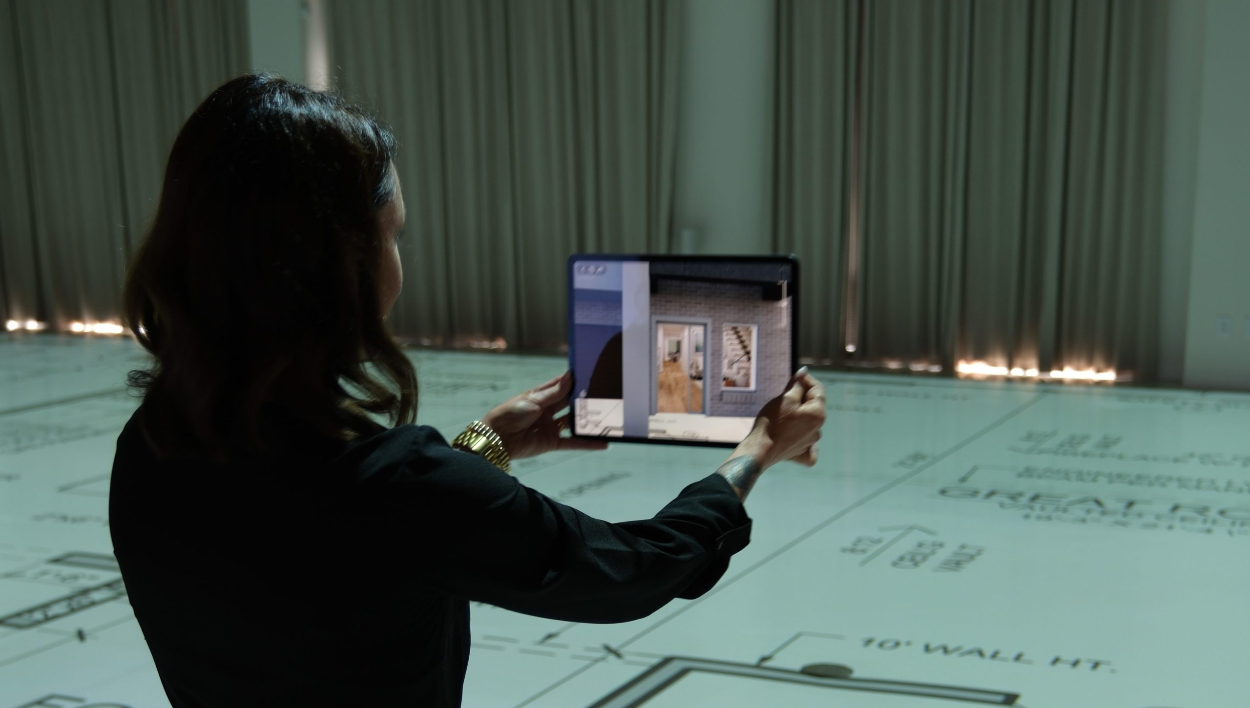 Woman using a tablet to view an augmented reality room rendering over a full-scale projected floor plan 