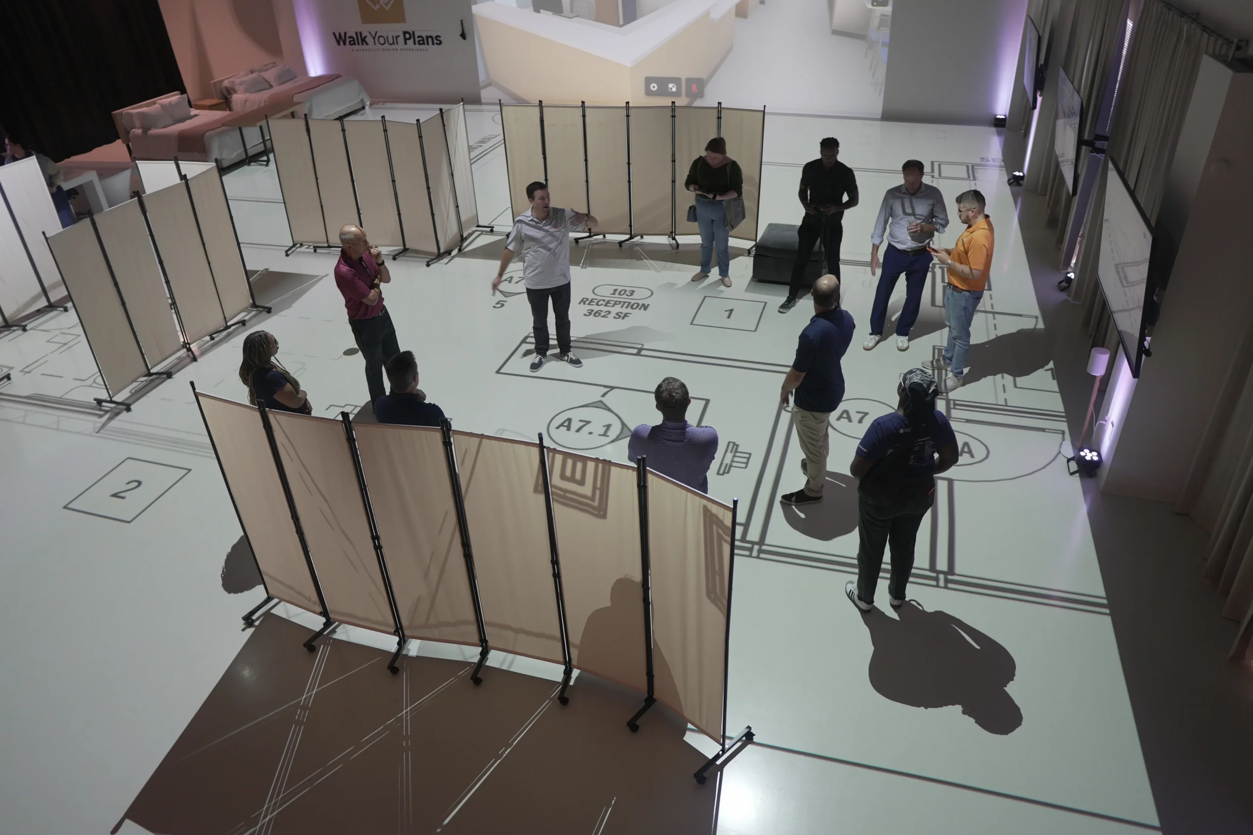 Group reviewing a full-scale projected floor plan with movable partition walls in the Walk Your Plans Nashville studio 