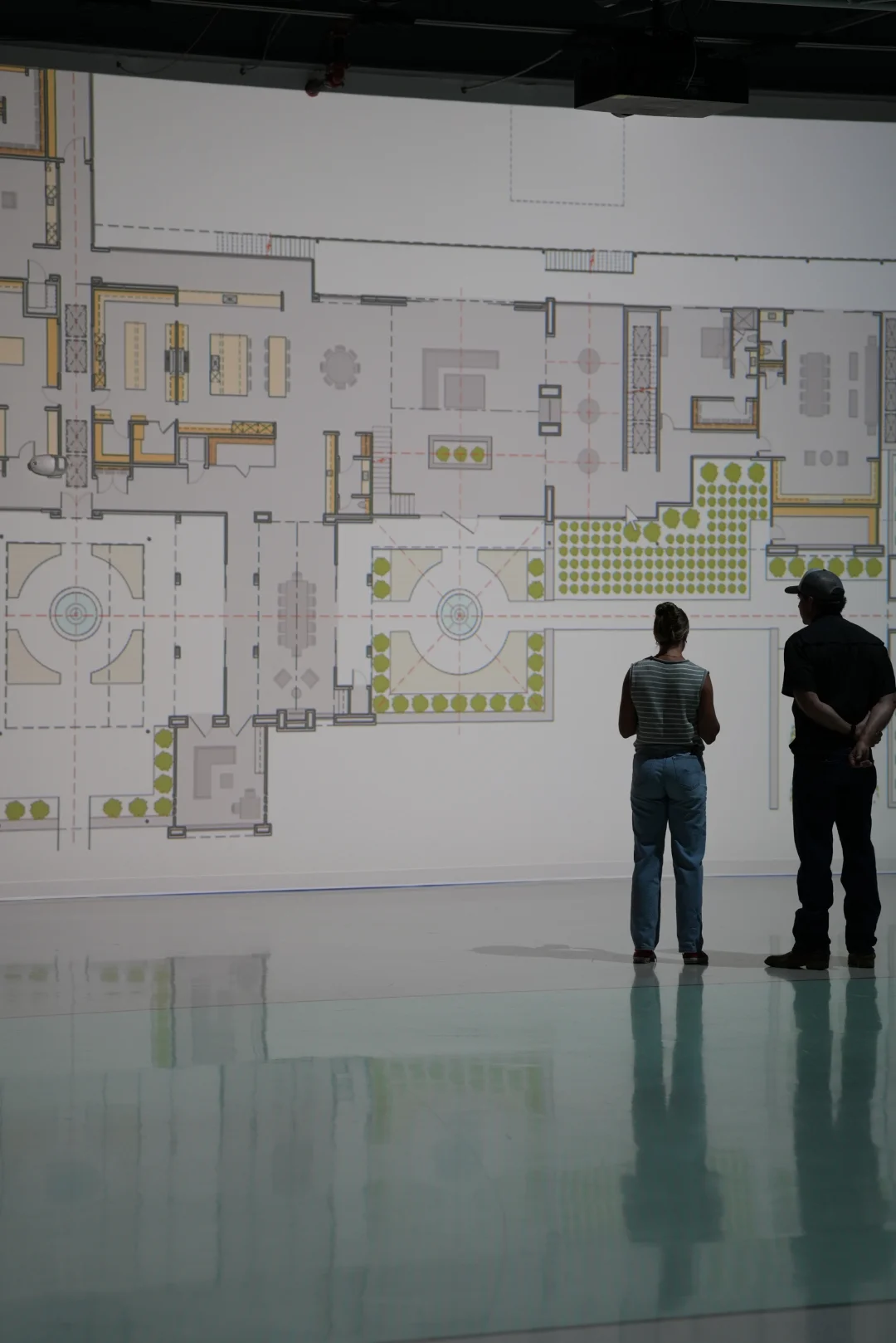 Two clients reviewing a color floor plan and site plan projected at full scale