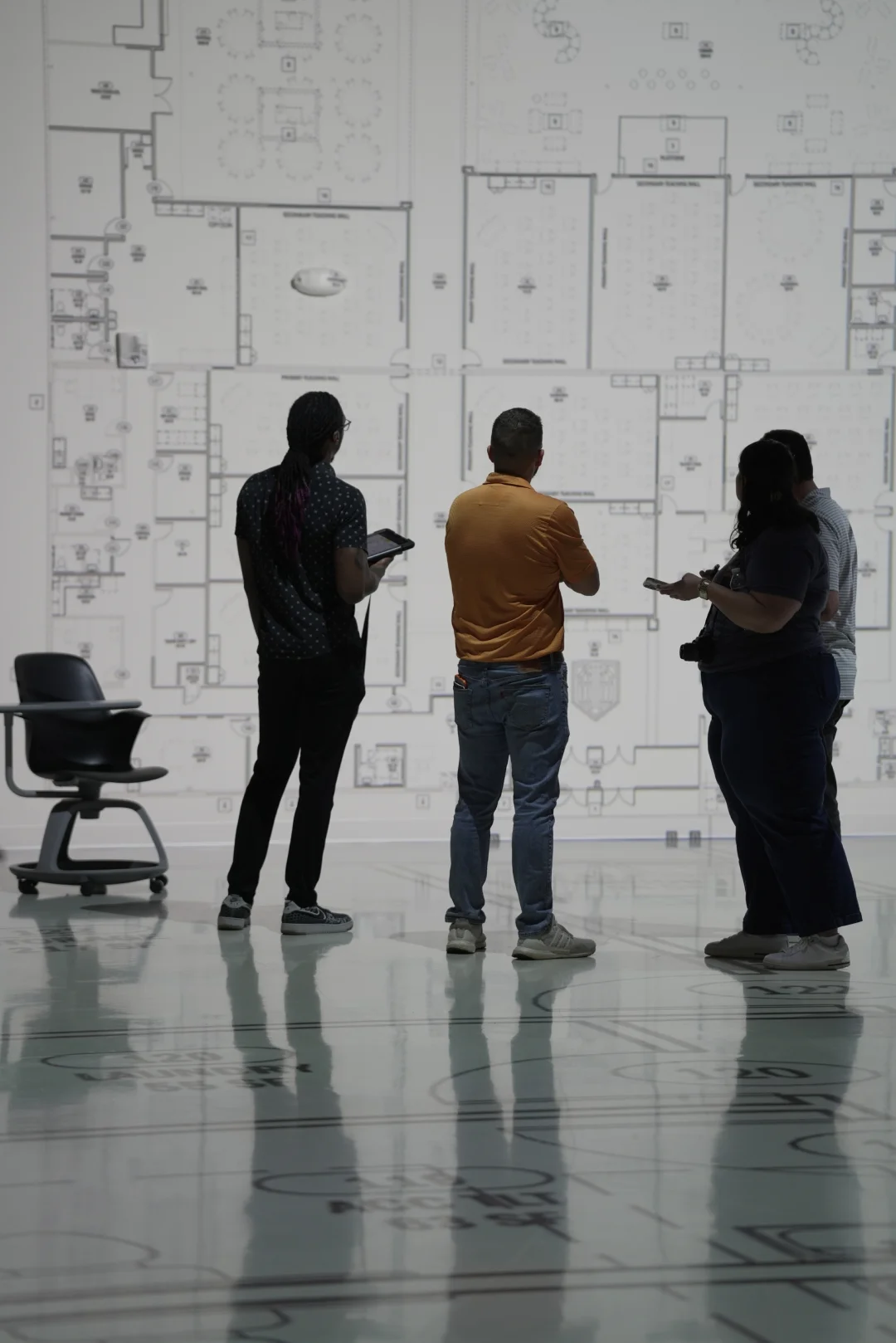 Team reviewing a wall-projected floor plan for a commercial project with a tablet during a guided walkthrough 