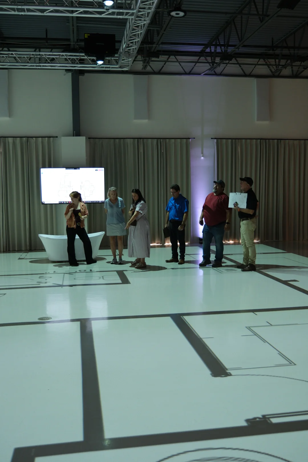 Group reviewing a floor plan on screen beside a staged bathroom projected at full scale