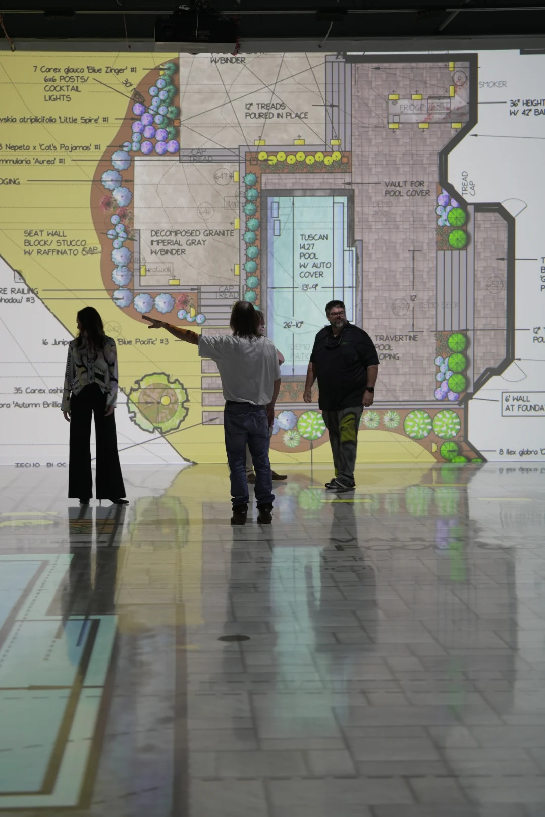 Clients reviewing a full-scale landscape and pool site plan projected on the studio wall. 