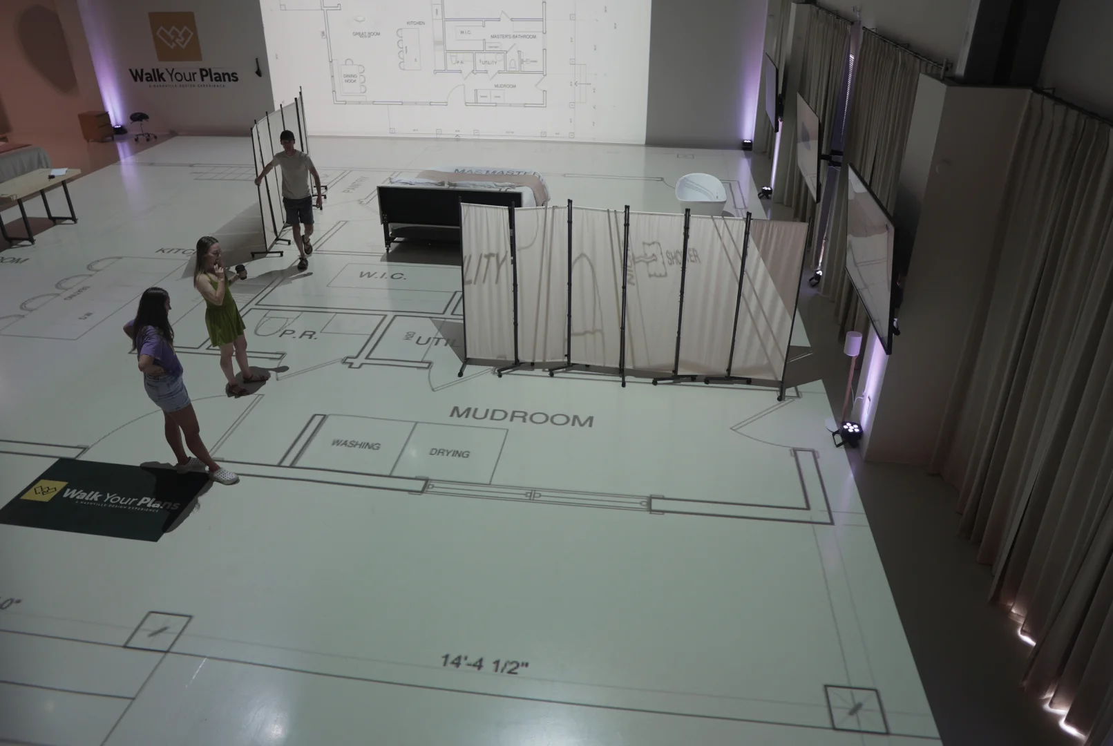 Team walking through a full-scale projected floor plan of a mudroom and bedroom layout with staged furniture